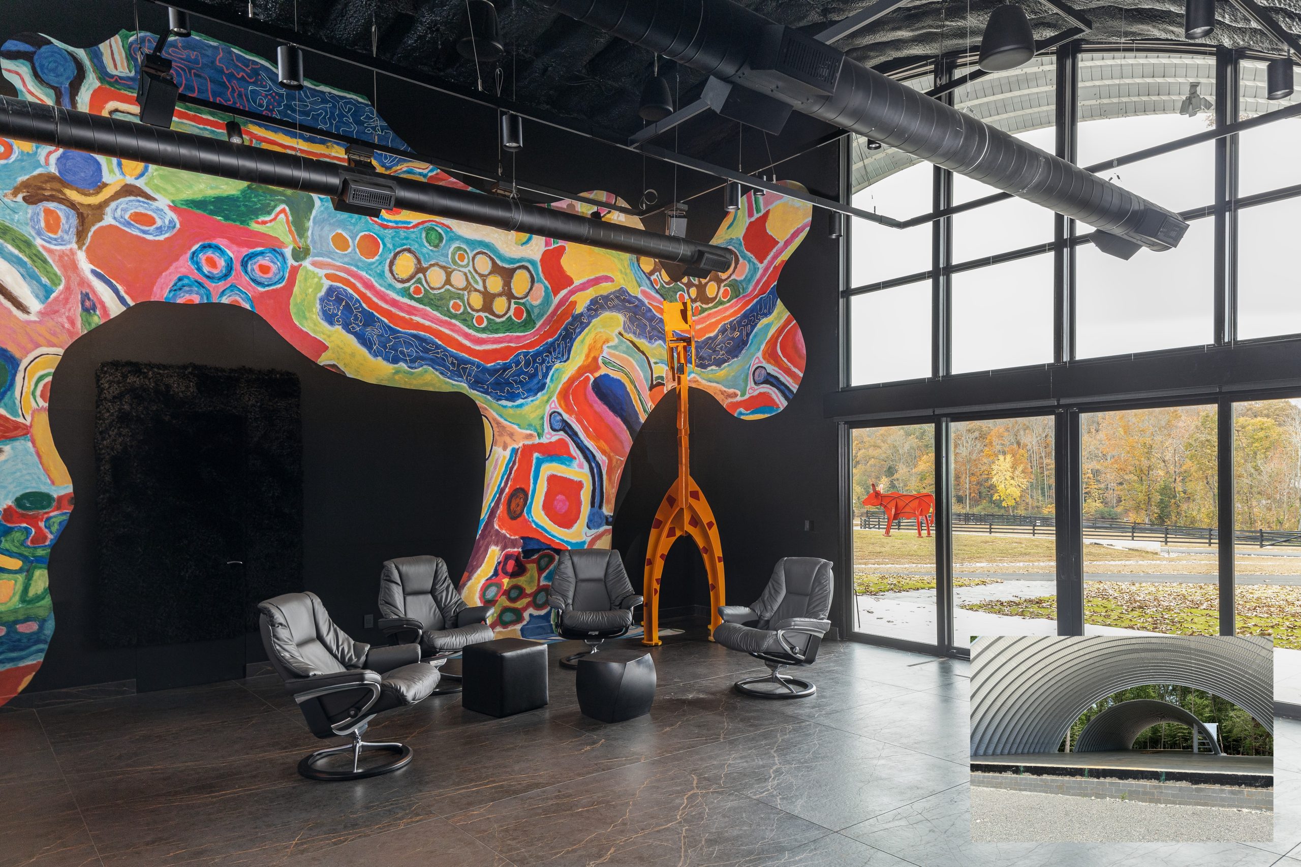 MMIS interior showroom with a colorful mural wall, black lounge chairs, industrial ceiling, large glass windows, and a sculptural orange doorway centerpiece.